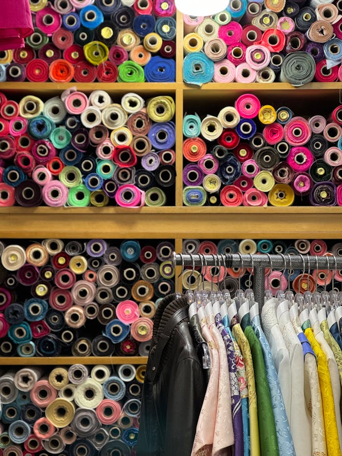 Colorful fabric rolls above clothes rack in tailor shop, capturing textile diversity.